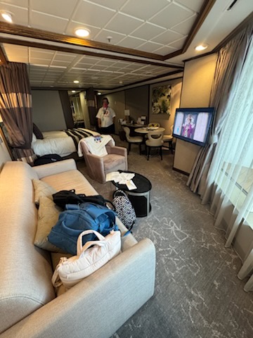 One-bedroom suite living area aboard the Norwegian Jewel with sofa, luggage, and steward preparing the room