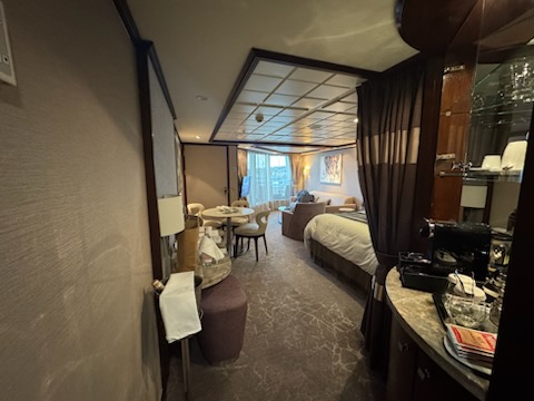 Bedroom and seating area in the Norwegian Jewel one-bedroom suite with balcony door and vanity