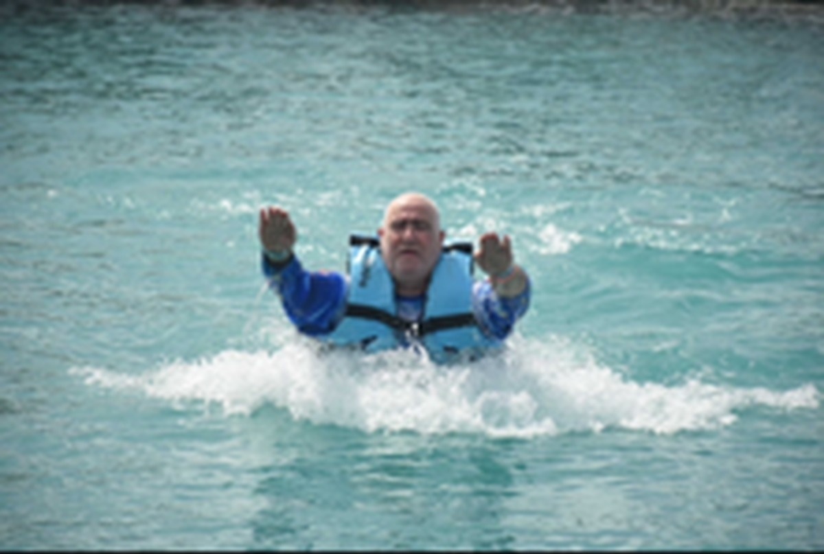Lawrence Brody with both arms raised in turquoise water and white foam during a Disney Fantasy dolphin push excursion — sequence 2 of 3
