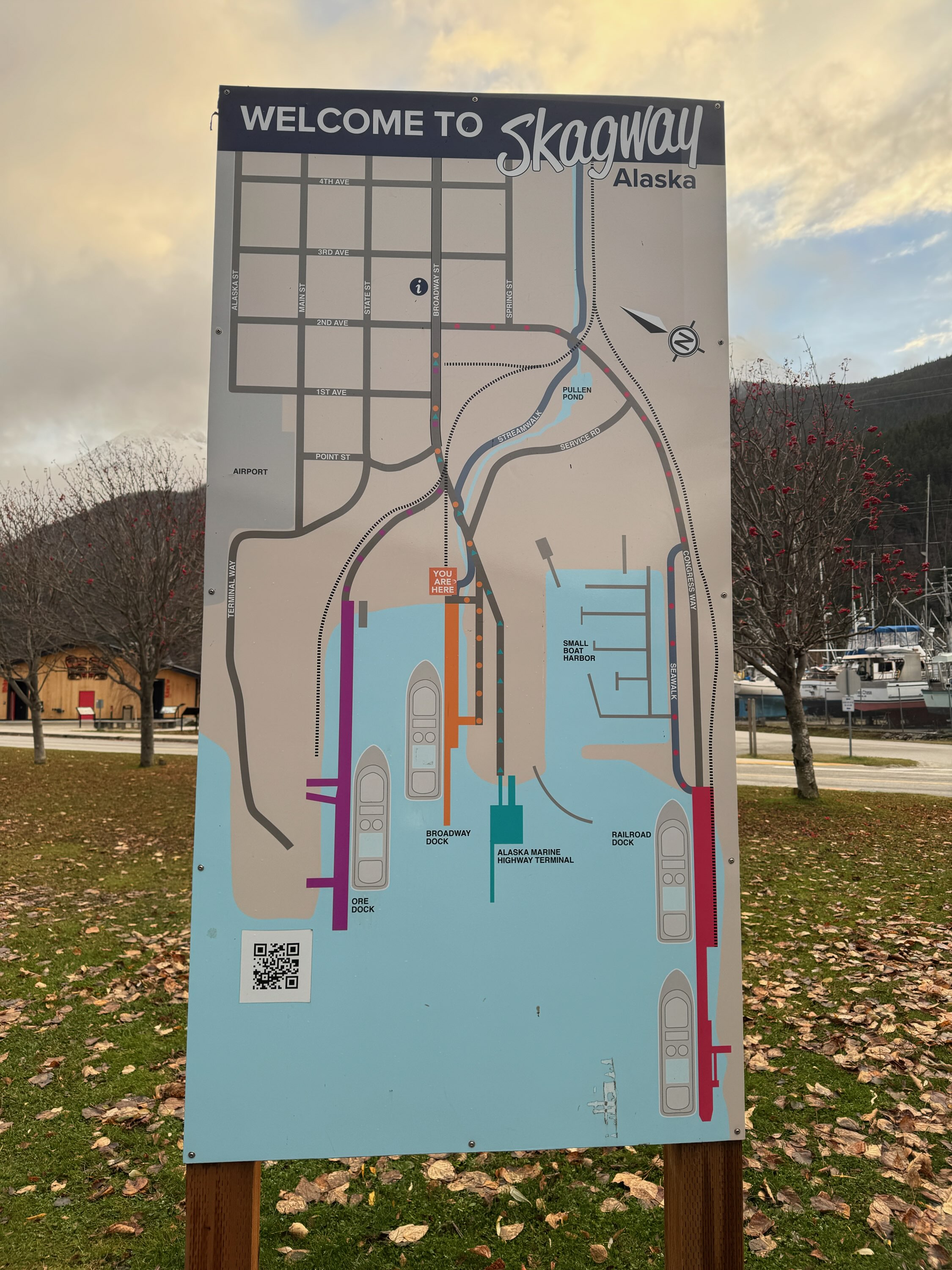 Outdoor Welcome to Skagway Alaska signboard with town map, docks, mountains, and marina behind it