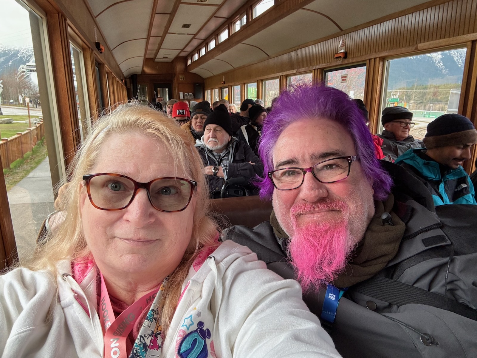 Lawrence and his wife smiling aboard the White Pass scenic train with snow-capped mountains outside the windows
