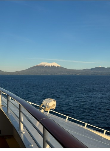 View from the bow of the Norwegian Jewel in Sitka, Alaska — ship railing, dark blue water, and snow-capped mountain range under a clear sky