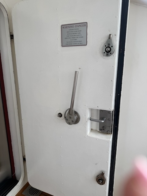 Heavy white marine watertight door with WARNING-DANGER placard leading to the bow-side balcony on the Norwegian Jewel